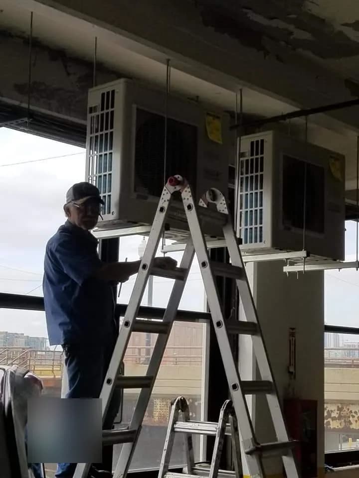 Ductless Heat Pump Installation — technician servicing suspended commercial mini-split outdoor units